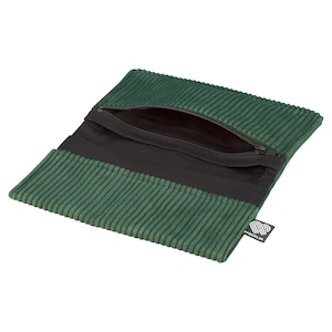 May include: Green corduroy pouch with a black zipper and interior. The pouch has a rectangular shape and a ribbed texture. A small black and white tag is attached to the side.