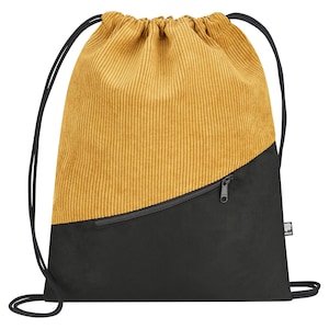Puede incluir: Mochila con cordón y diseño bicolor. La parte superior es de pana mostaza y la inferior negra. Cuenta con un bolsillo con cremallera negro.