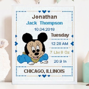 May include: A framed cross-stitch featuring a smiling Minnie Mouse in blue. The text includes the name "Jonathan Jack Thompson", date, time, weight (7 lbs 8 oz), and height (20.9 in) at birth, and location "Chicago, Illinois".