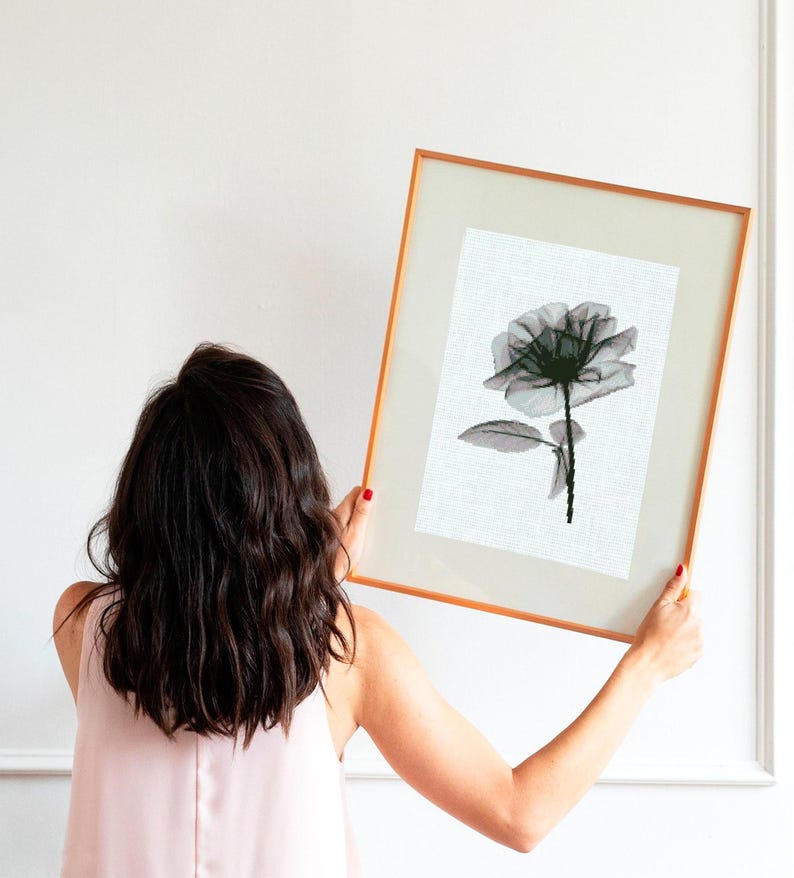 May include: A framed art print featuring a black and white floral illustration of a rose. The artwork is displayed in a gold-toned frame with a white mat. The image is held up against a white wall.