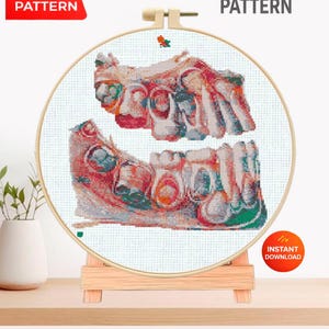 May include: A cross stitch pattern displayed in a round wooden embroidery hoop on a small wooden stand. The design features a detailed anatomical illustration of human teeth and gums in shades of red, white, and blue. Text reads PDF PATTERN, CROSS STITCH PATTERN, and INSTANT DOWNLOAD.