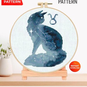 May include: A cross-stitch pattern featuring a blue silhouette of a bull with a constellation design. The design is displayed in a wooden embroidery hoop. Text on the image reads "PDF PATTERN" and "CROSS STITCH PATTERN".
