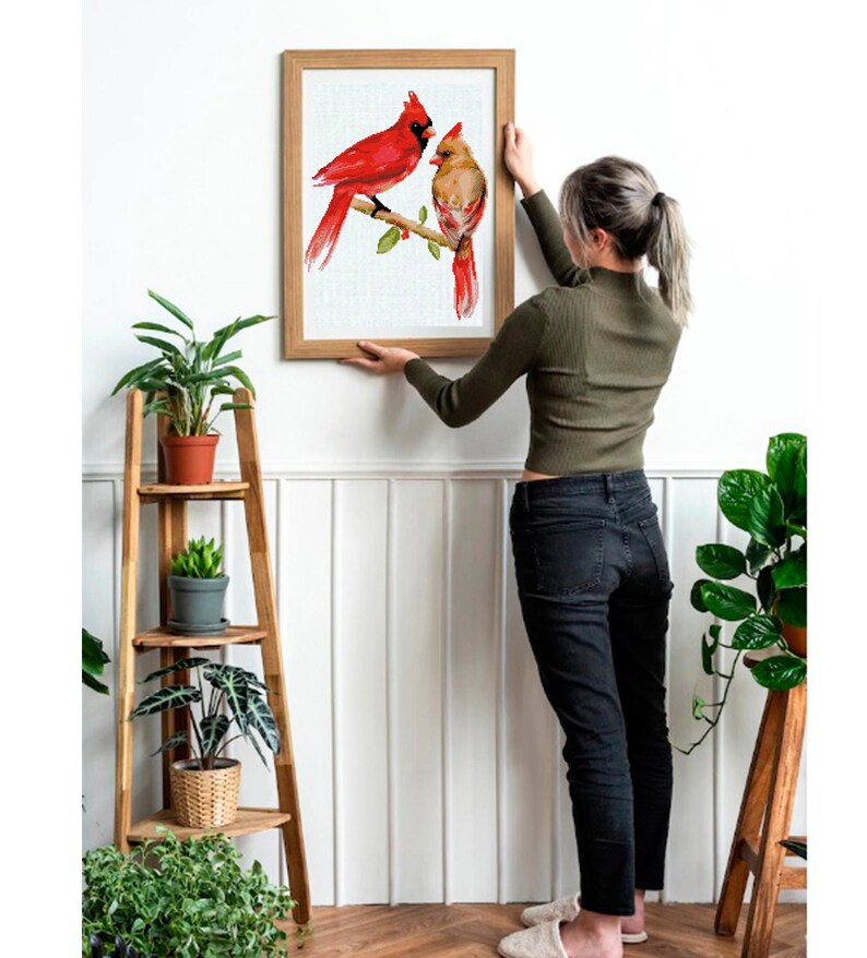 May include: A framed watercolor print of two red cardinal birds perched on a branch. The artwork features a male and female cardinal with detailed feather textures and a naturalistic style. The frame is a light brown color.
