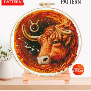 May include: A cross-stitch pattern depicting a bull's head, the Taurus constellation, and its symbol. The design is in a round embroidery hoop, displayed on a wooden stand. Text on the image reads "PDF PATTERN" and "CROSS STITCH PATTERN".