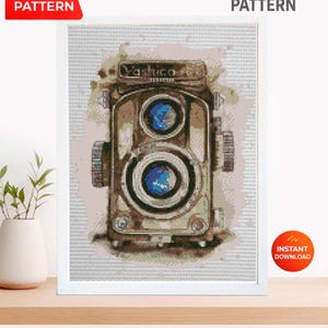 May include: Cross stitch pattern of a vintage Yashica camera. The artwork features a detailed, pixelated image of the camera in shades of brown, beige, and blue, set against a light background. The words "PDF Pattern" and "Instant Download" are also visible.