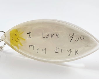 May include: A white resin keychain shaped like a boat with a yellow sun drawing and the words "I love you from Etyk" written in black ink.