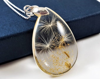 Puede incluir: Un collar con un colgante de plata en forma de lágrima relleno de resina transparente que contiene semillas de diente de león y purpurina dorada.