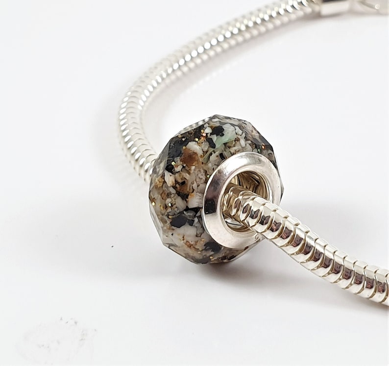 May include: A silver charm bracelet with a faceted glass bead filled with black, white, and brown sand-like material.