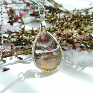 May include: A silver chain necklace with a teardrop-shaped pendant. The pendant is filled with a clear resin and contains a dried dandelion with gold flecks.