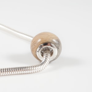 May include: A silver charm bracelet with a round bead made of hair. The bead is inscribed with the name "Frank".