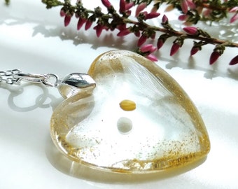 May include: A heart-shaped pendant necklace with a clear resin filled with gold glitter and a small yellow flower. The pendant is attached to a silver chain.