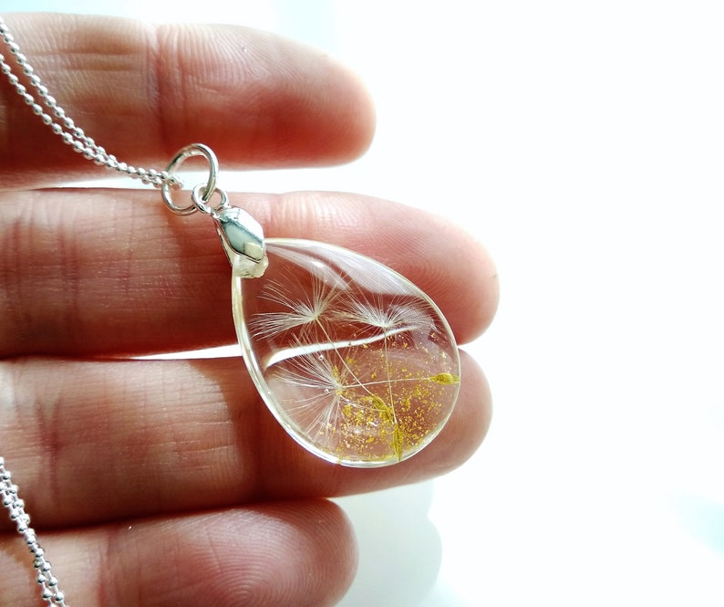 May include: A silver chain necklace with a teardrop-shaped pendant containing a preserved dandelion seed head. The pendant is clear and shows the delicate white seeds and golden pollen.
