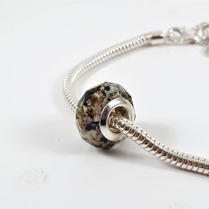 May include: A silver charm bracelet with a black, white, and gold speckled charm bead.