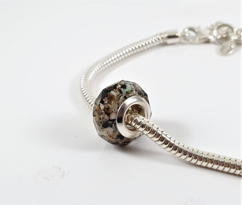 May include: A silver charm bracelet with a black, white, and gold speckled charm bead.