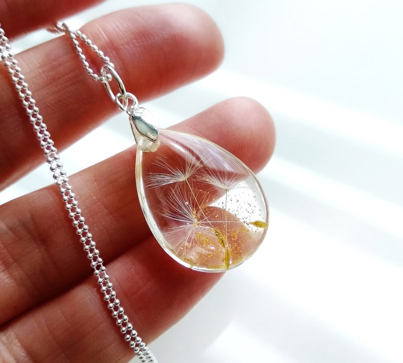 May include: A silver chain necklace with a teardrop-shaped pendant containing a preserved dandelion. The pendant is clear and shows the dandelion's white seeds and golden pollen.