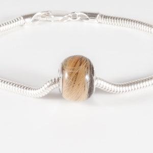 May include: A silver bracelet with a round bead filled with brown and blonde hair.