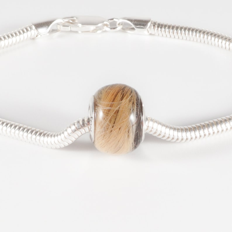 May include: A silver bracelet with a round bead filled with brown and blonde hair.