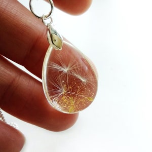 May include: A silver necklace with a teardrop-shaped pendant containing a preserved dandelion with gold glitter.
