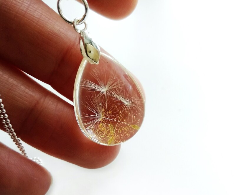 May include: A silver necklace with a teardrop-shaped pendant containing a preserved dandelion with gold glitter.