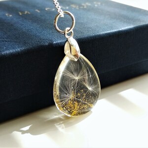 May include: A silver teardrop-shaped pendant necklace with a clear resin charm containing a dried dandelion with gold glitter.