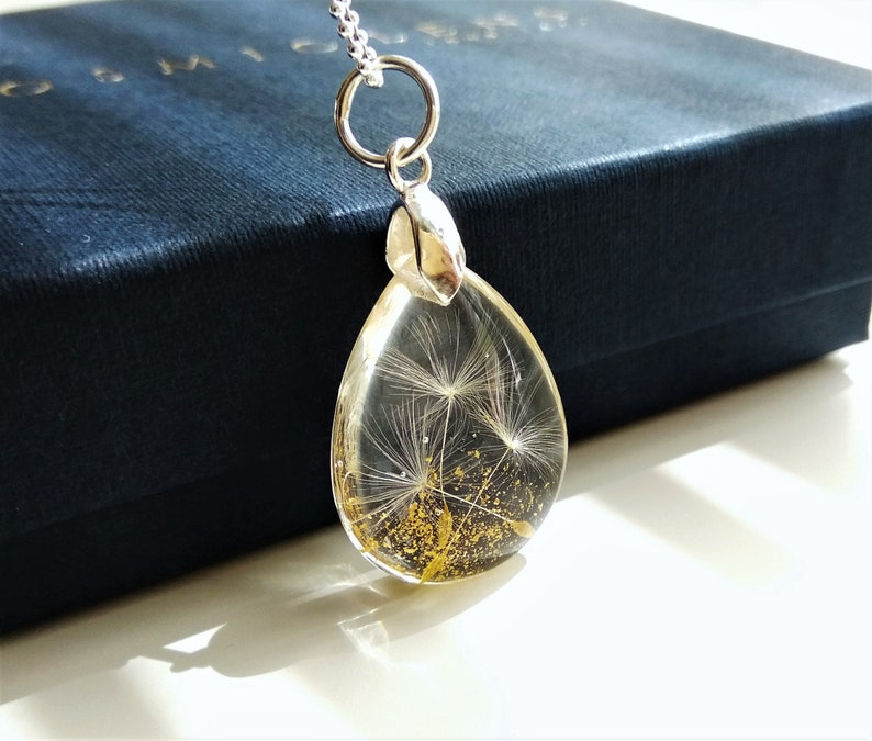 May include: A silver teardrop-shaped pendant necklace with a clear resin charm containing a dried dandelion with gold glitter.