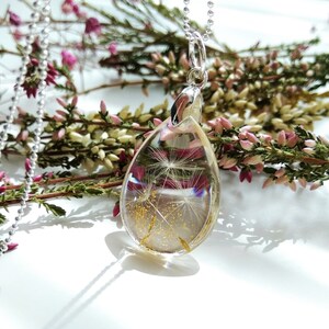 May include: A silver chain necklace with a teardrop-shaped pendant. The pendant is filled with clear resin and contains a dried dandelion with gold glitter.