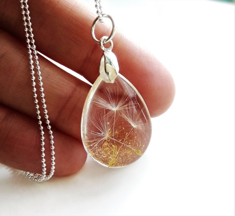 May include: A silver chain necklace with a teardrop-shaped pendant. The pendant is filled with a clear resin and contains a dried dandelion with gold glitter.
