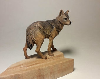 May include: A hand-carved wooden wolf figurine standing on a wooden base. The wolf is brown and gray with a detailed face and fur.