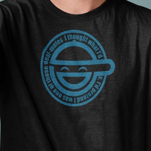 Puede incluir: Un hombre con una camiseta negra con un gráfico azul de una cara sonriente con una línea sobre los ojos y el texto "I poured one out for the real mutes I thought what'd I do".