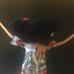 May include: A handmade doll with black hair and a floral dress. The doll has outstretched arms and is made of felt and fabric.