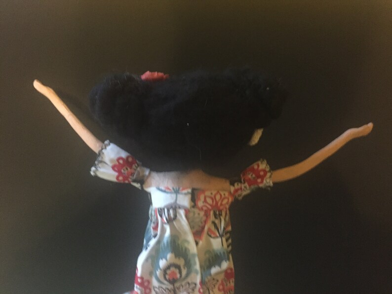May include: A handmade doll with black hair and a floral dress. The doll has outstretched arms and is made of felt and fabric.