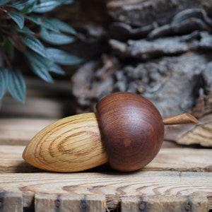 May include: A wooden acorn-shaped box with a lid. The box is made from two different types of wood, one light brown and one dark brown. The box is resting on a wooden surface.