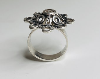 May include: A silver ring with a geometric design featuring a central circle surrounded by smaller circles and triangles.