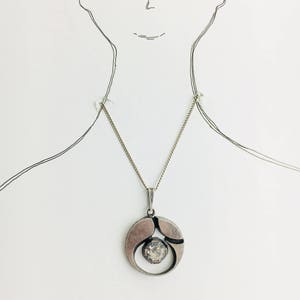 May include: A silver necklace with a geometric pendant featuring a clear crystal stone.