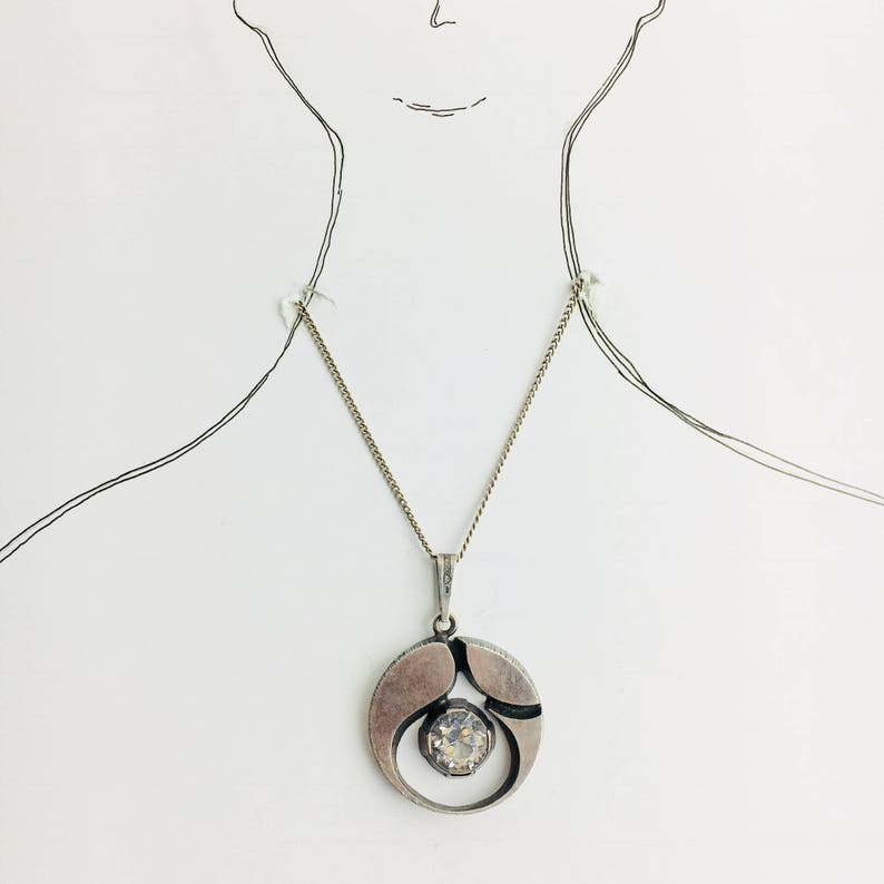 May include: A silver necklace with a geometric pendant featuring a clear crystal stone.