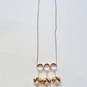May include: A gold necklace with three open circles and three dangling pearl-like ornaments.