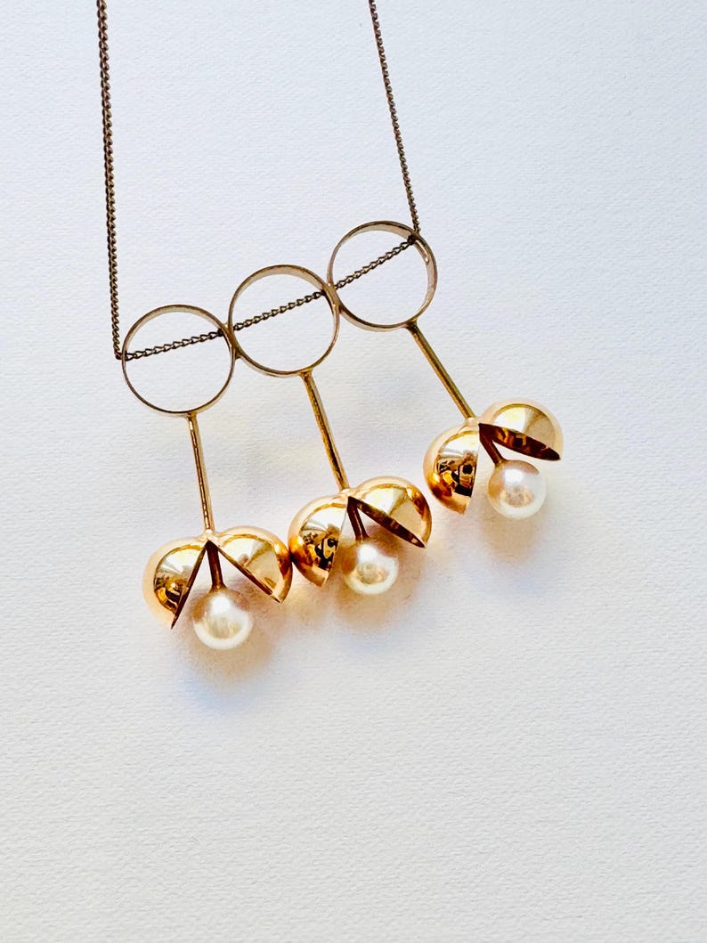 May include: Gold necklace with three open circles and three dangling gold spheres with pearls inside.