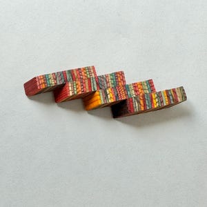 Puede incluir: Un conjunto de cuatro bloques de madera coloridos apilados en forma de escalera. Los bloques están hechos de madera con un patrón en capas de diferentes colores, incluyendo rojo, naranja, amarillo, verde, azul y morado.
