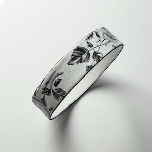 May include: A white ceramic bangle with a black and white floral design.