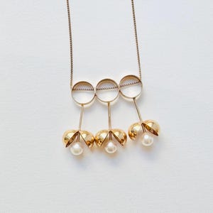 May include: A gold necklace with three open circles and three pearl-like pendants hanging from the circles.