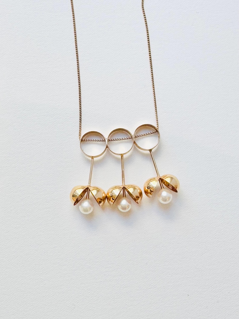 May include: A gold necklace with three open circles and three pearl-like pendants hanging from the circles.