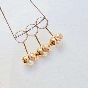 May include: A gold necklace with three interlocking circles and four dangling gold spheres, each containing a pearl.