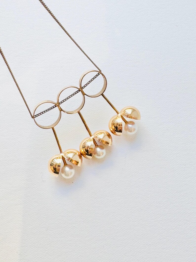 May include: A gold necklace with three interlocking circles and four dangling gold spheres, each containing a pearl.