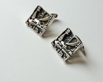 May include: A pair of silver cufflinks with a textured, abstract design. The cufflinks are square shaped and have a silver finish.