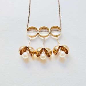 May include: A gold necklace with three interlocking circles and three dangling pearl-like spheres.
