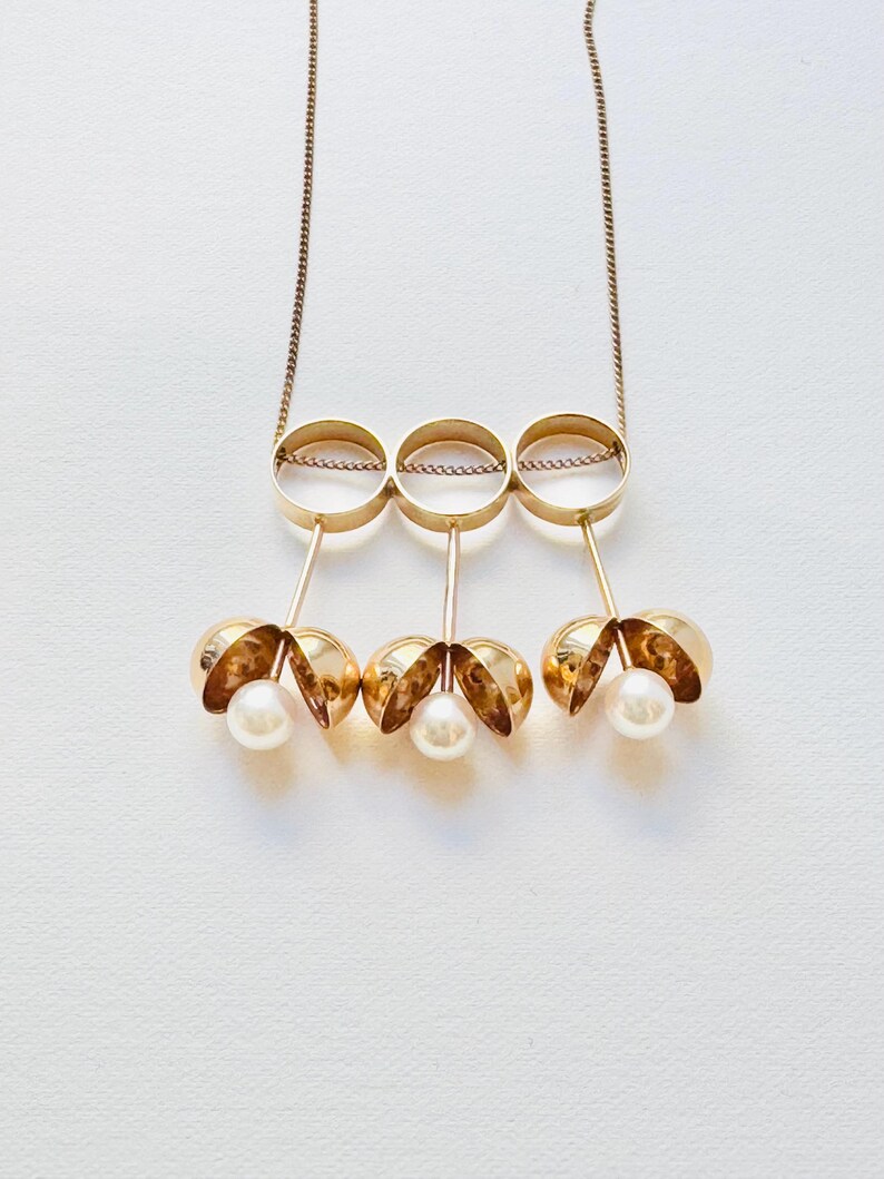 May include: A gold necklace with three interlocking circles and three dangling pearl-like spheres.