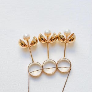 May include: A gold ring with three pearl-topped spheres attached to a chain. The spheres are open on one side, revealing the pearl inside.