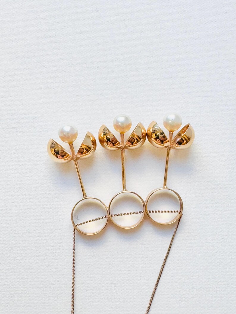 May include: A gold ring with three pearl-topped spheres attached to a chain. The spheres are open on one side, revealing the pearl inside.