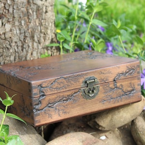 May include: A wooden box with a dark brown finish and a decorative tree branch design. The box has a brass latch and hinges.