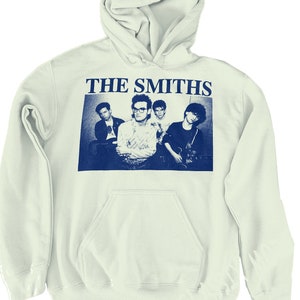 May include: A white hooded sweatshirt with a blue print of the band The Smiths. The print features a black and white photo of the band members.